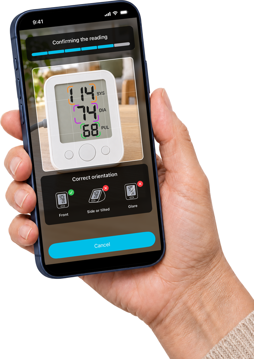 An iPhone held in hand, scanning a blood pressure monitor showing 114 systolic, 74 diastolic, and a pulse of 68